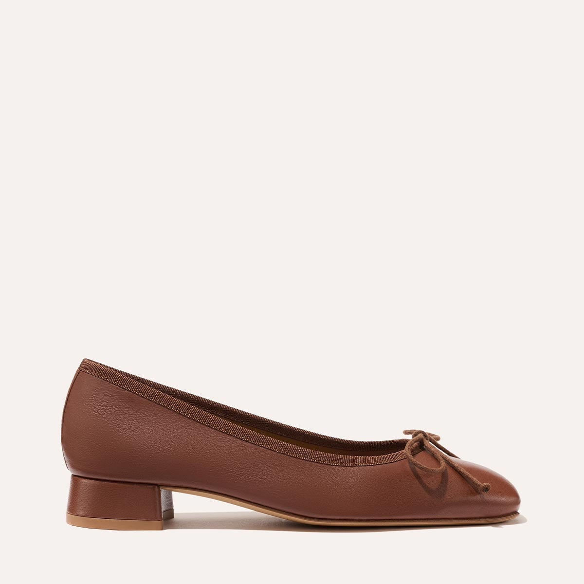 The Ada - Cognac Nappa by margaux-development is a brown leather ballet pump with a low block heel, rounded toe, and front bow. Sacchetto construction ensures a glove-like fit. Shown in side profile on a plain light background.