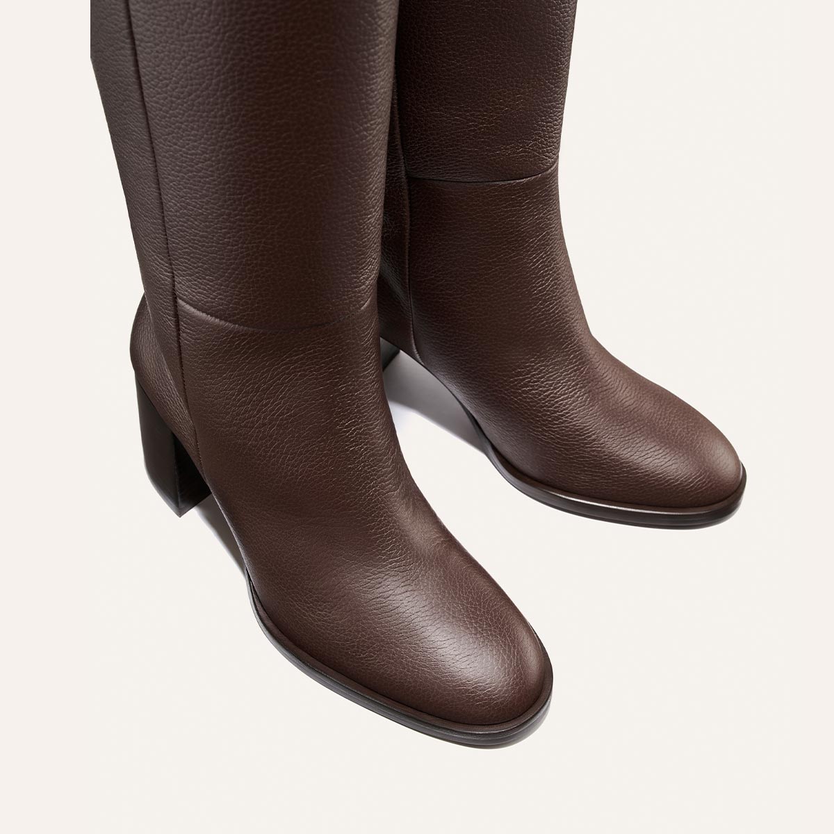 The Alison Roman x Margaux Charlie Boot in brown tumbled calf by Margaux is featured here—a pair of textured, knee-high boots with block heels, displayed from a slightly angled top view against a light background.