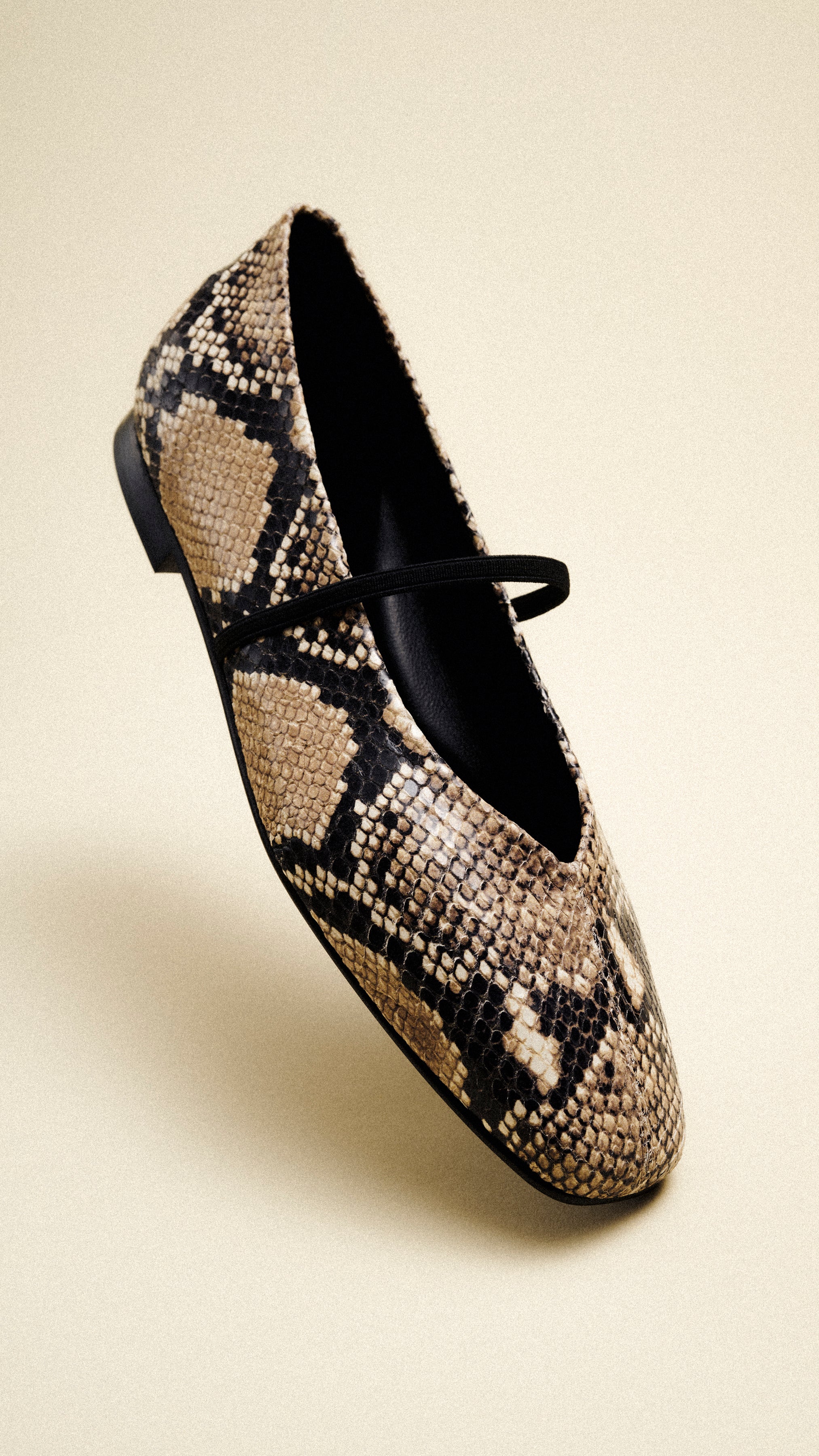 A single flat shoe with a brown and black snakeskin pattern and a thin black strap across the top, displayed on a neutral beige background.