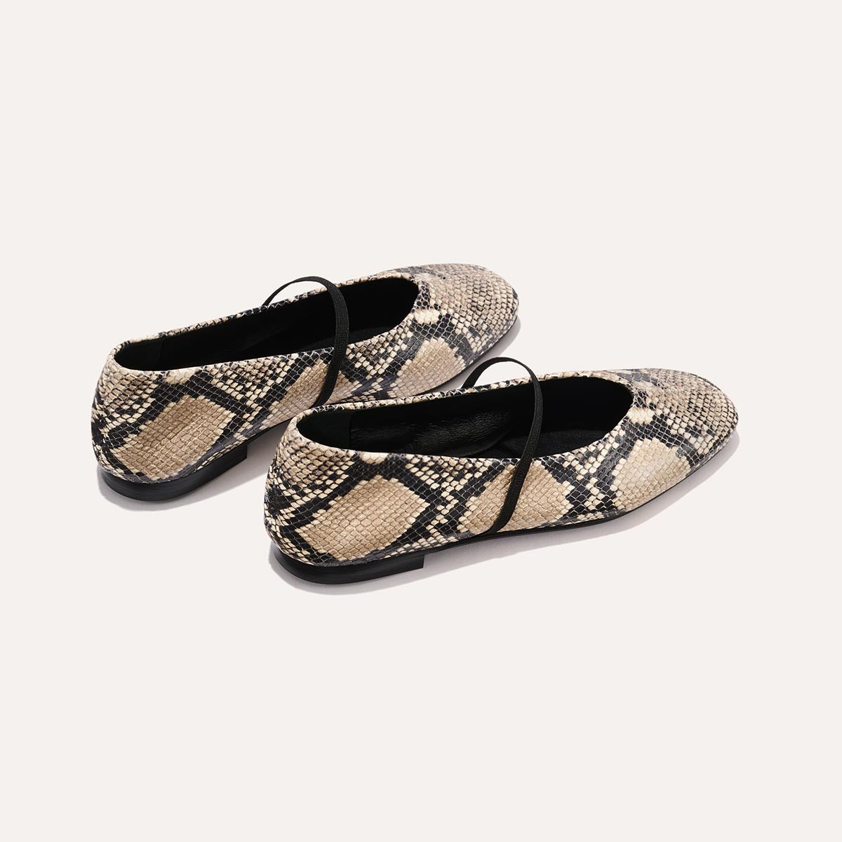 The Phoebe - Natural Python Embossed by margaux-development: deconstructed flat Mary Jane shoes in beige and black python emboss, featuring black soles and thin black straps, shown on a plain light background.