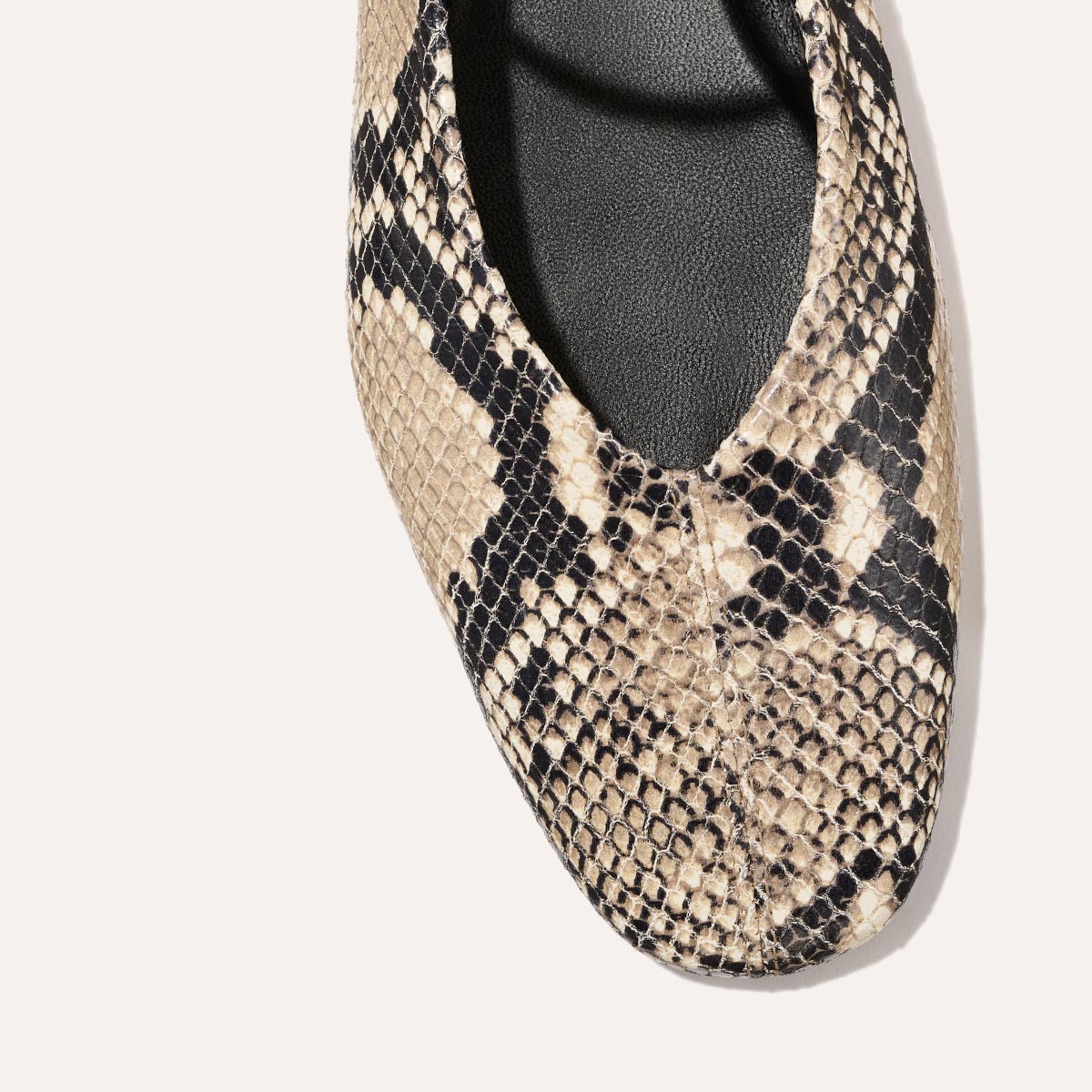 Close-up of the toe area of The Phoebe - Natural Python Embossed flat by margaux-development, showing its rounded shape, visible stitching, and sacchetto construction in black and beige python embossing on a white background.