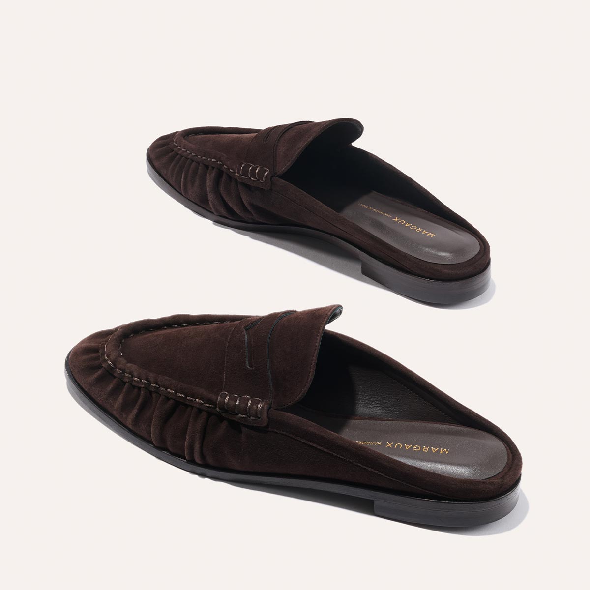 The Astor Loafer Mule in Espresso Suede by margaux-development features a ruched side design and branded insole, shown against a light background.