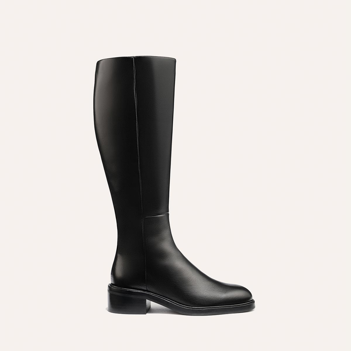 The Margaux City Boot - Black Calf features a tall, black leather knee-high design with a low heel and round toe, offering a sleek, minimal look that channels the classic riding boot silhouette. Displayed against a plain light background.