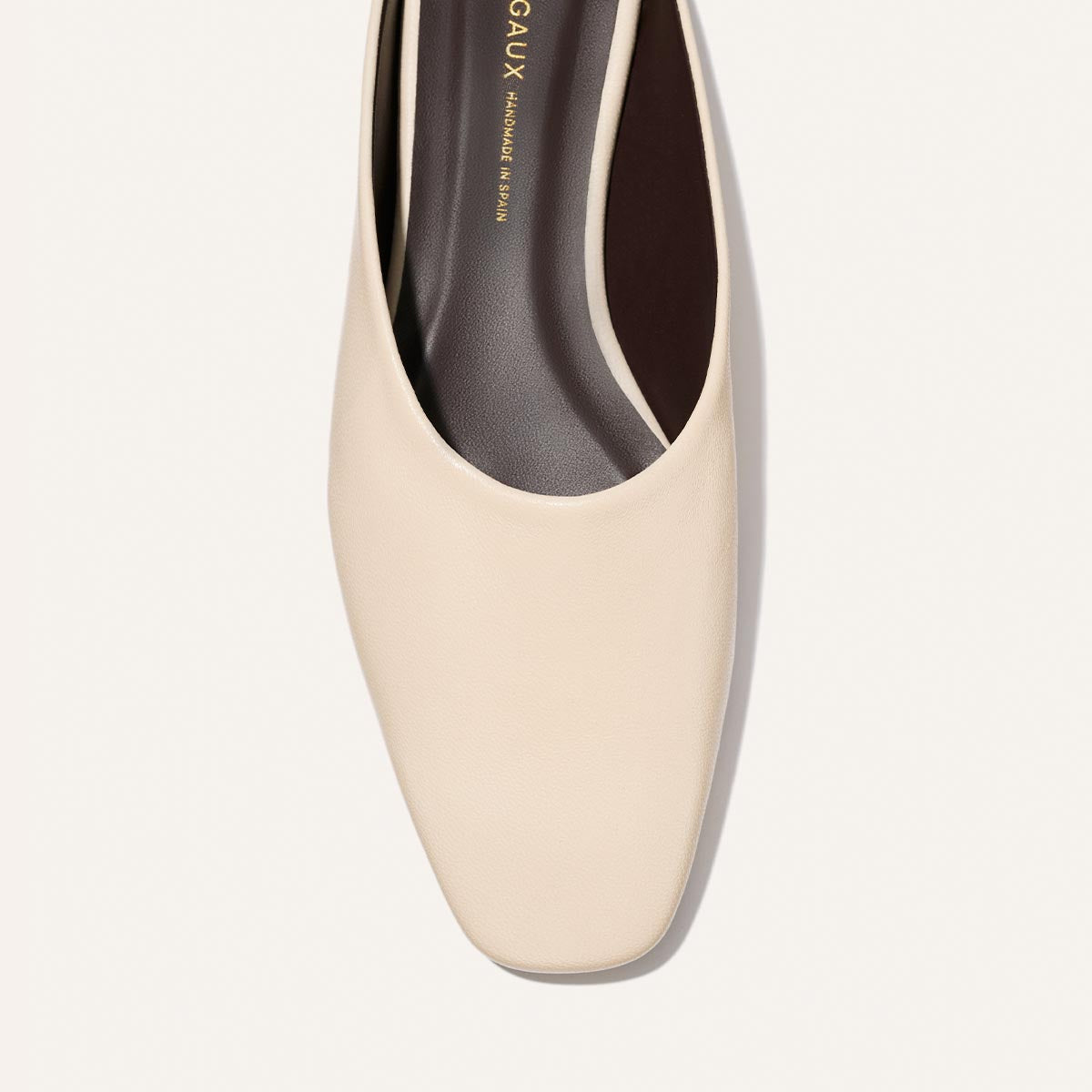 A top-view close-up of Margaux’s The Clara - Bone Nappa, a cream-hued square-toe flat with a smooth finish and dark brown insole, set against a light backdrop.