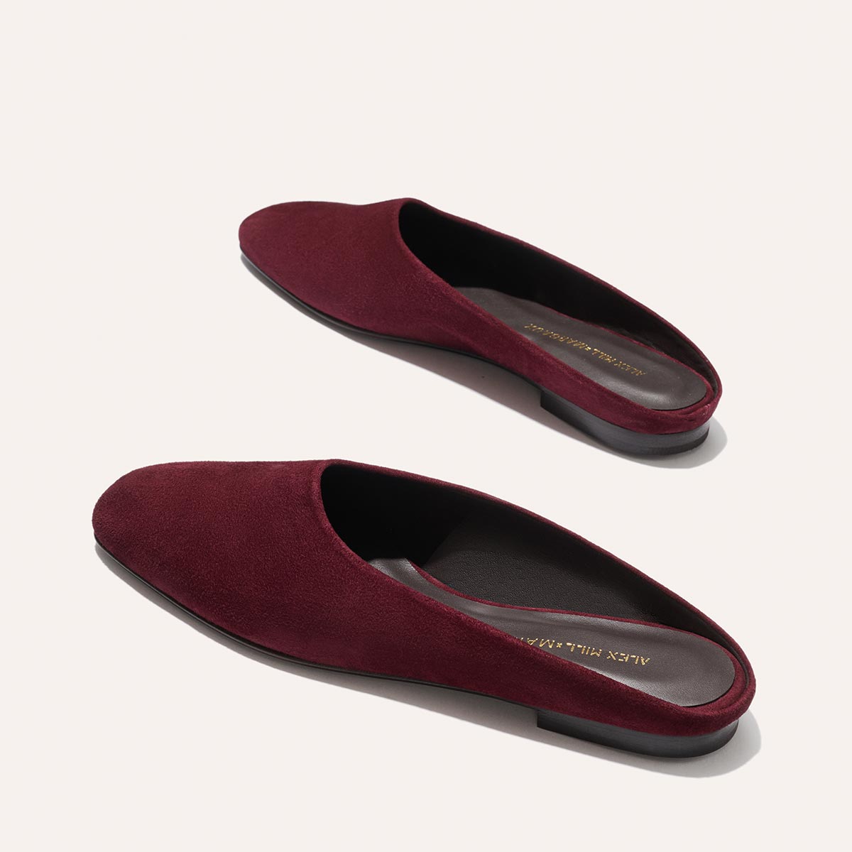 The Clara - Burgundy Suede by Margaux: slip-on, flat suede mules from the Alex Mill x Margaux collection with closed, rounded toes and black soles offer versatile style on a light background.