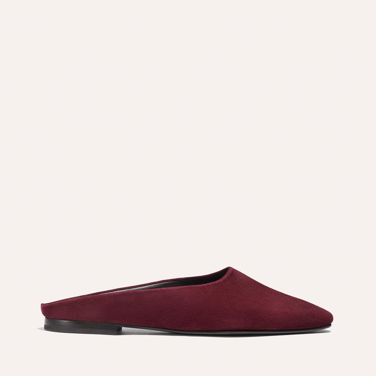 The Margaux Alex Mill x Margaux: The Clara - Burgundy Suede is a slip-on mule with a flat black sole, shown in profile against a light background, highlighting the stylish versatility of flat shoes.