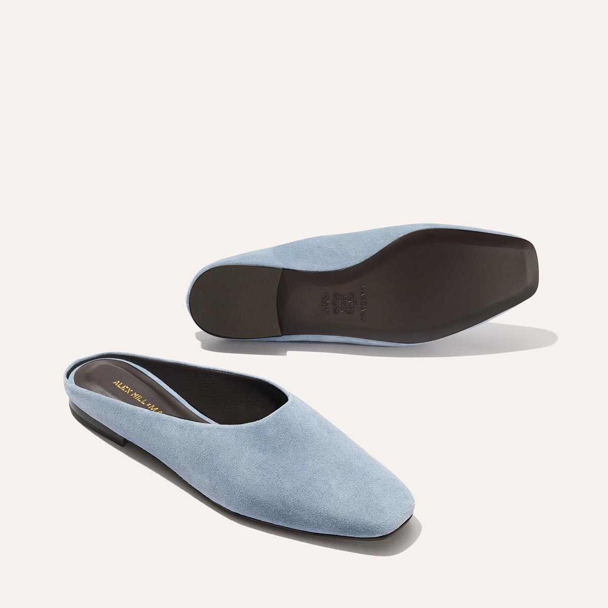 The Clara in Slate Blue Suede by Margaux (Alex Mill x Margaux) features light blue suede, square toes, low black heels, and a dark sole—one upright and one sole-up—styled for chic versatility against a light background.