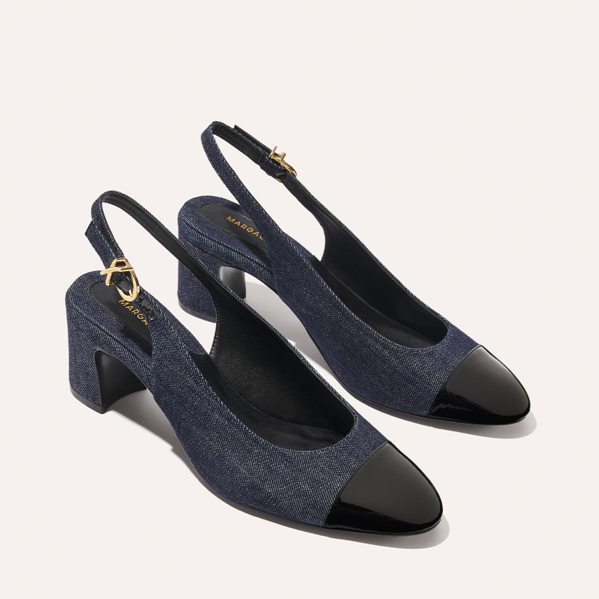 The Cluny Slingback by margaux-development features indigo denim, black patent cap toes, chunky heels, and gold buckles—a stylish womens pump perfect for elevating your work shoe collection.