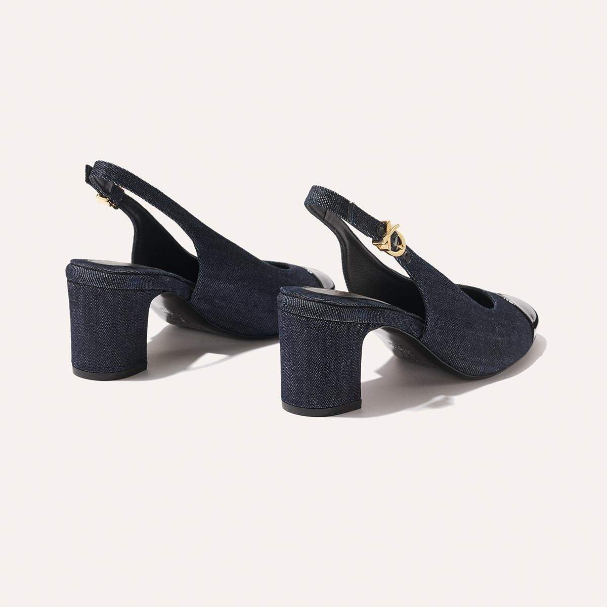 The Cluny Slingback by margaux-development features indigo denim and patent, open toes, block heels, and gold buckle ankle straps—an elegant staple—shown on a light background.