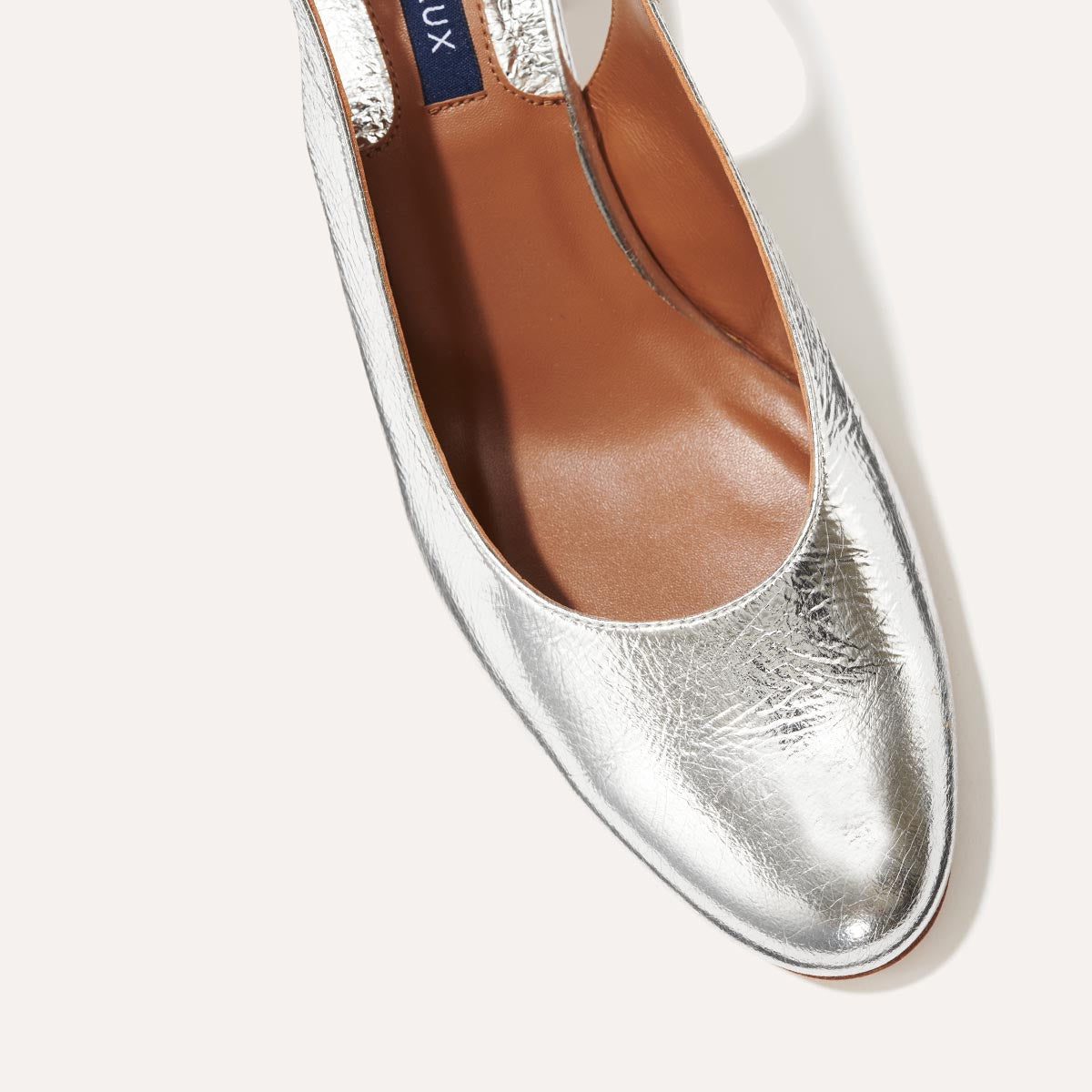 The Cluny Slingback in shiny Silver Crinkle Nappa, featuring a sleek Italian nappa leather upper with an adjustable buckle and a comfortable 2.5-inch black heel.