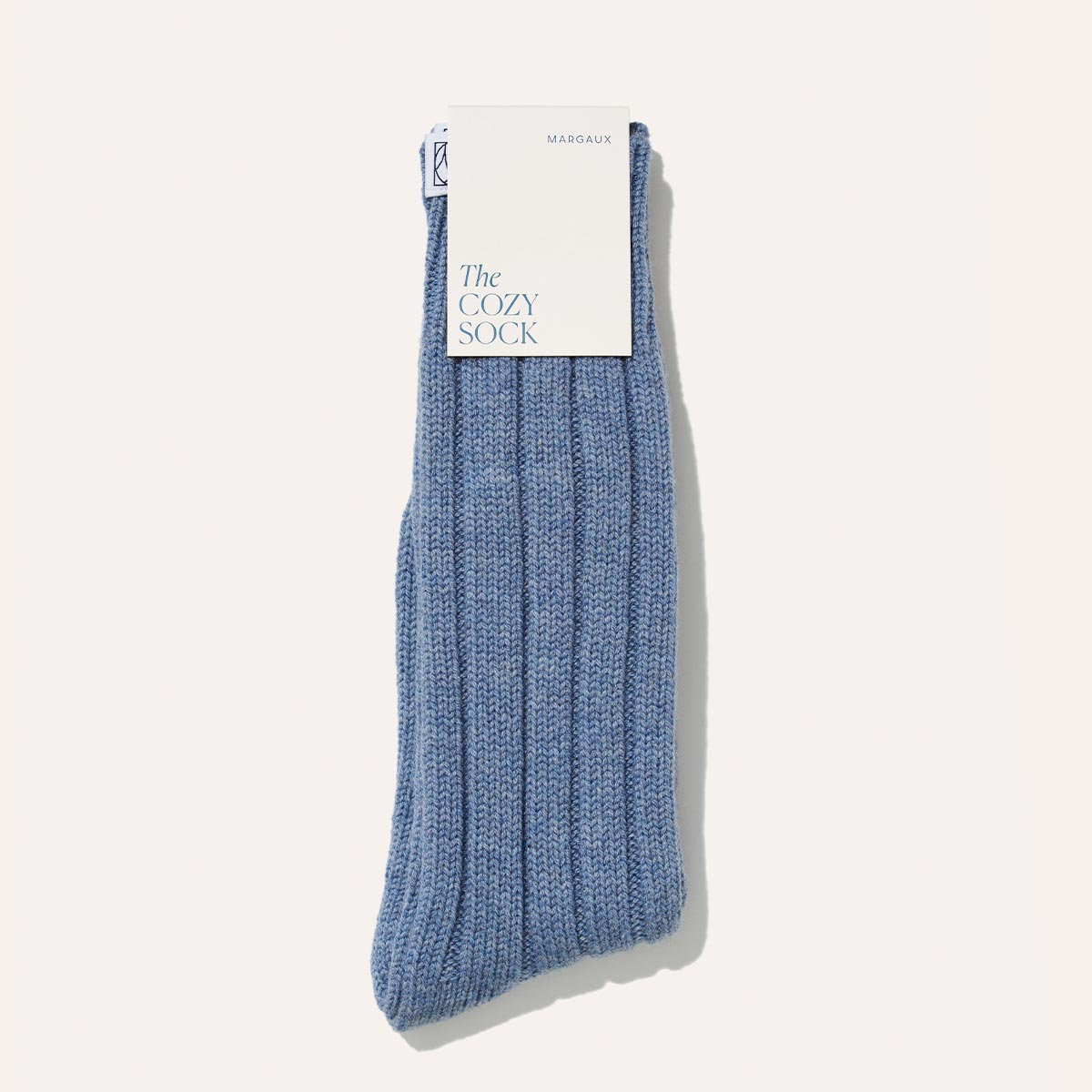 A pair of The Cozy Sock - Light Blue Wool / Cashmere Blend by Margaux, folded neatly with a white tag, offers super-soft luxury for lounging.