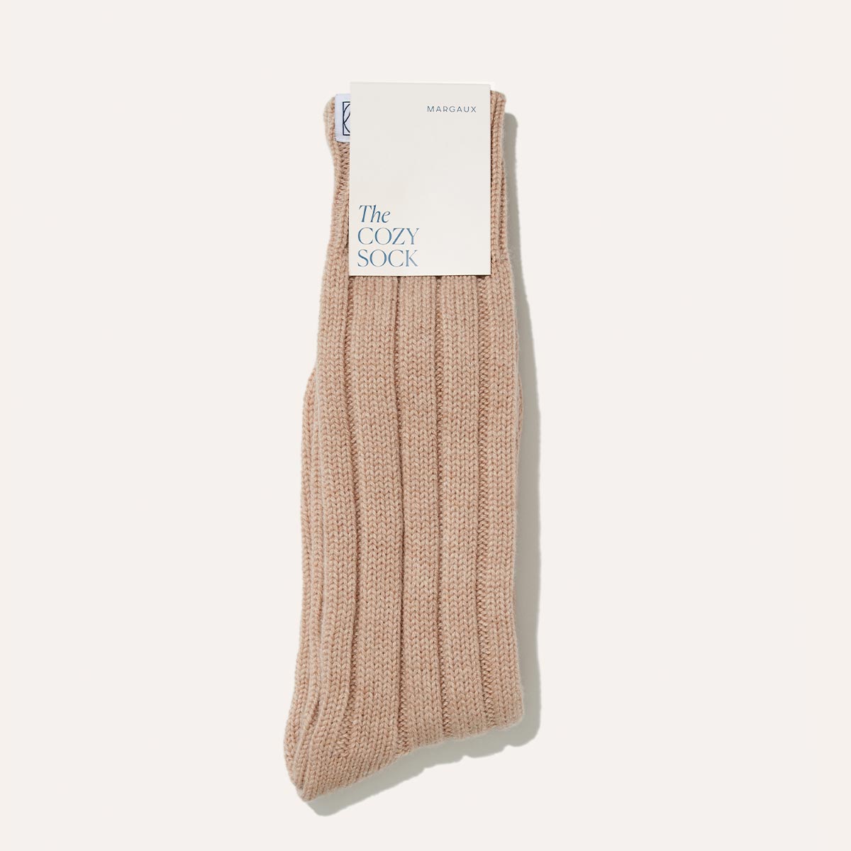 A single Margaux Cozy Sock in oatmeal wool-cashmere blend is shown against a white background with a tag reading Margaux The Cozy Sock—ideal for luxurious lounging.