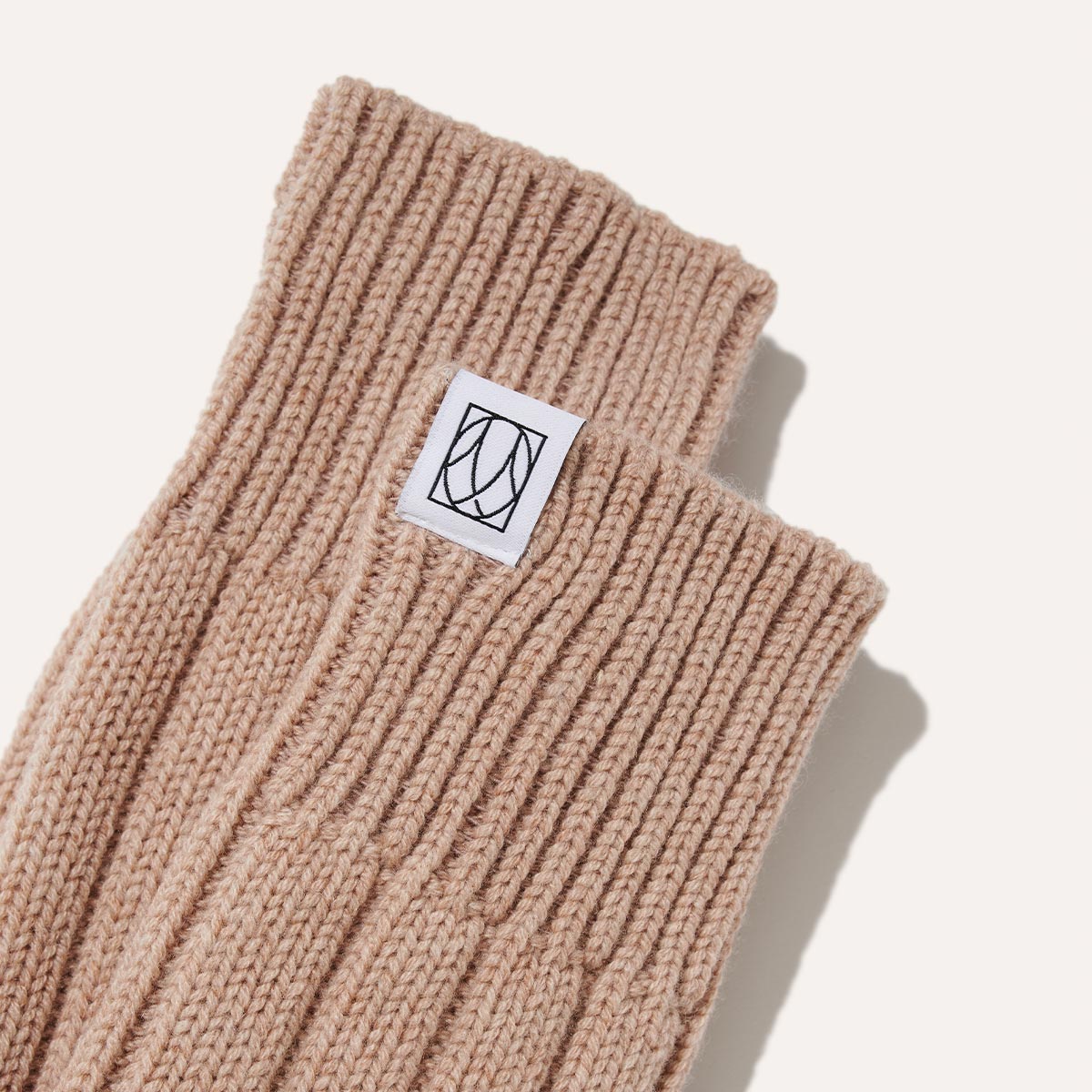 The Cozy Sock by Margaux in an oatmeal wool-cashmere blend features a white patch with a black geometric logo—ultra-soft and perfect for luxurious lounging, shown on a plain light background.