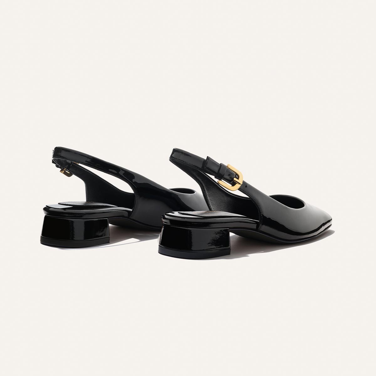 The Darcy Slingback - Black Patent by Margaux features adjustable straps, low block heels, and gold buckle details. This ballet pump-inspired shoe is perfect for warm weather, shown here on a light background.