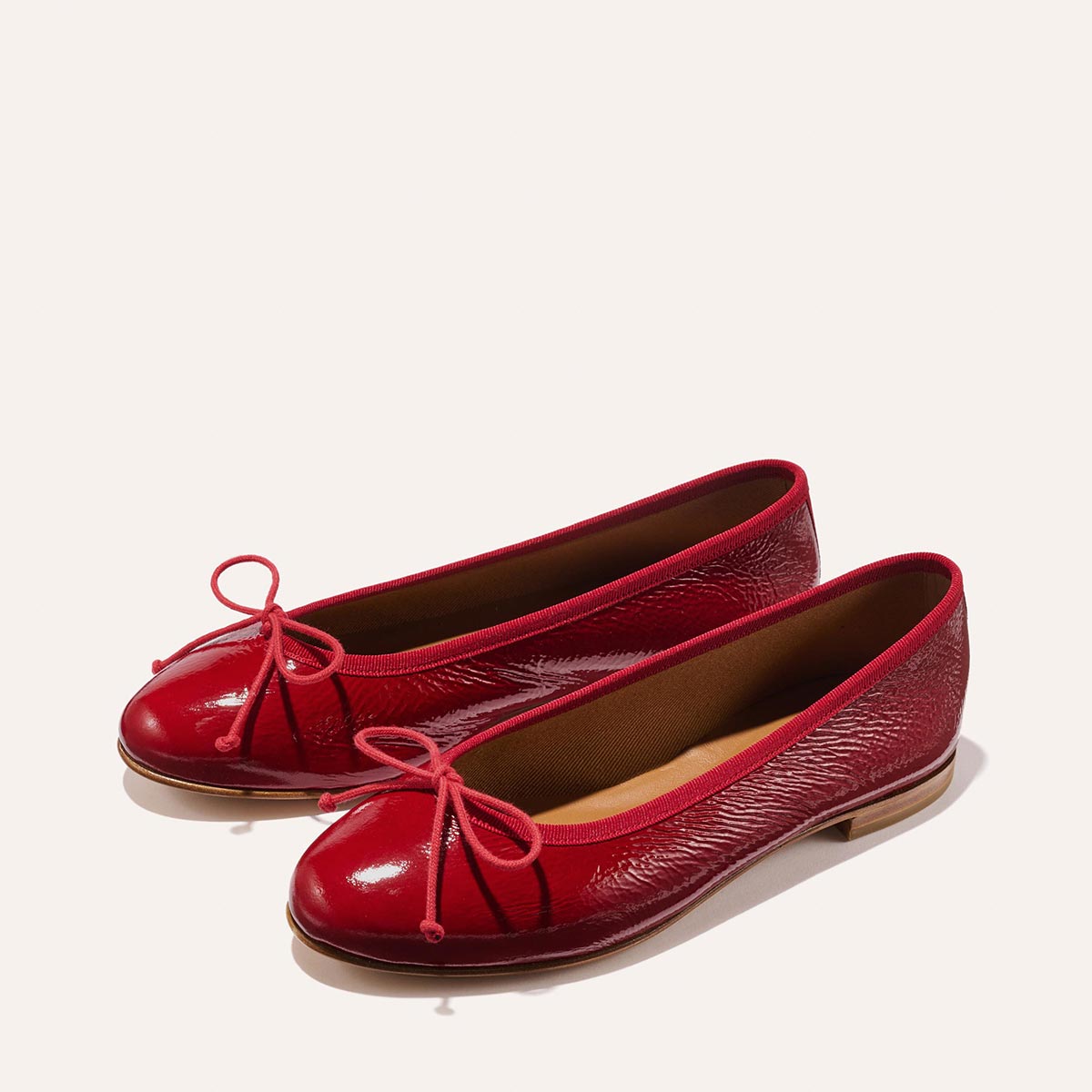 The Demi - Berry Crinkle Patent by margaux-development: shiny red ballet flats with rounded toes, small front bows, and low wooden heels, shown against a light background.