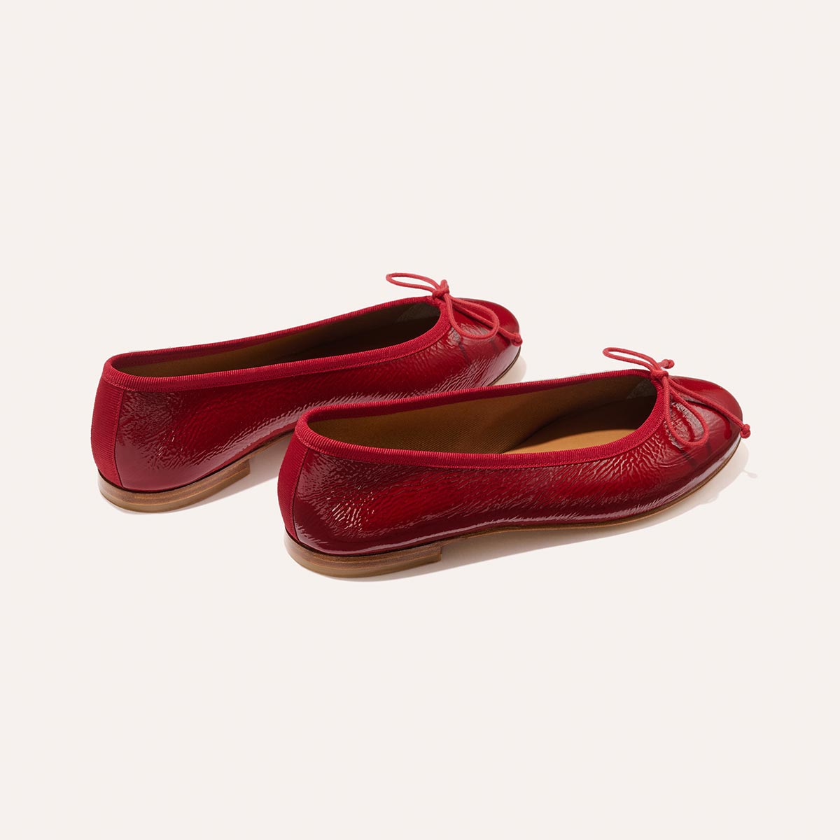 The Demi - Berry Crinkle Patent by margaux-development: shiny red ballet flats with small bows on the front, displayed on a light background.
