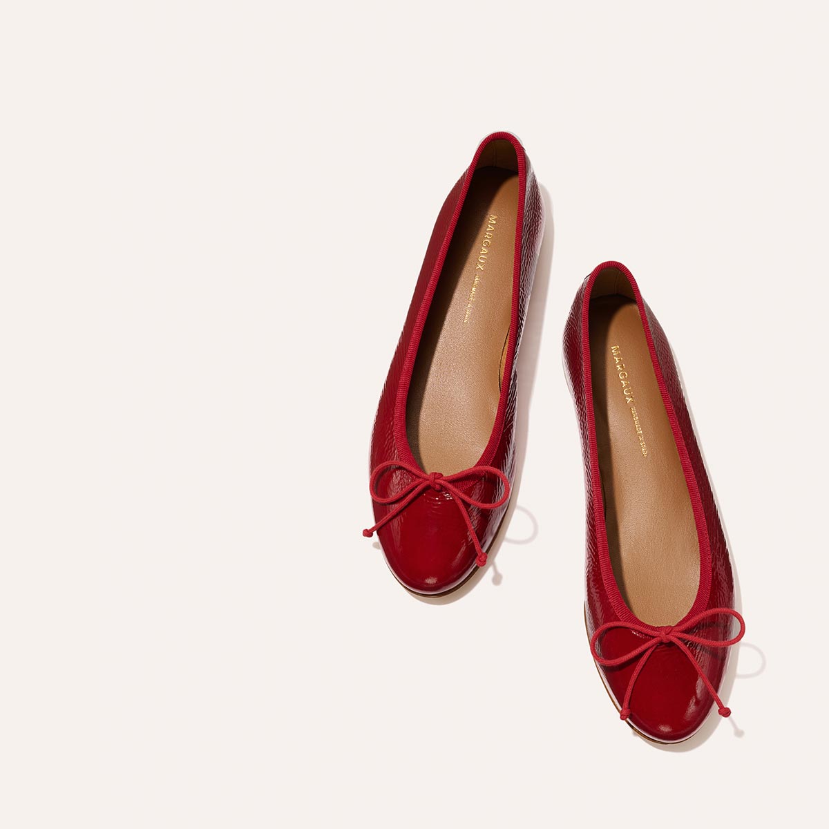 The Demi - Berry Crinkle Patent by margaux-development: glossy red ballet flats with bow details on the toes, shown against a light background.