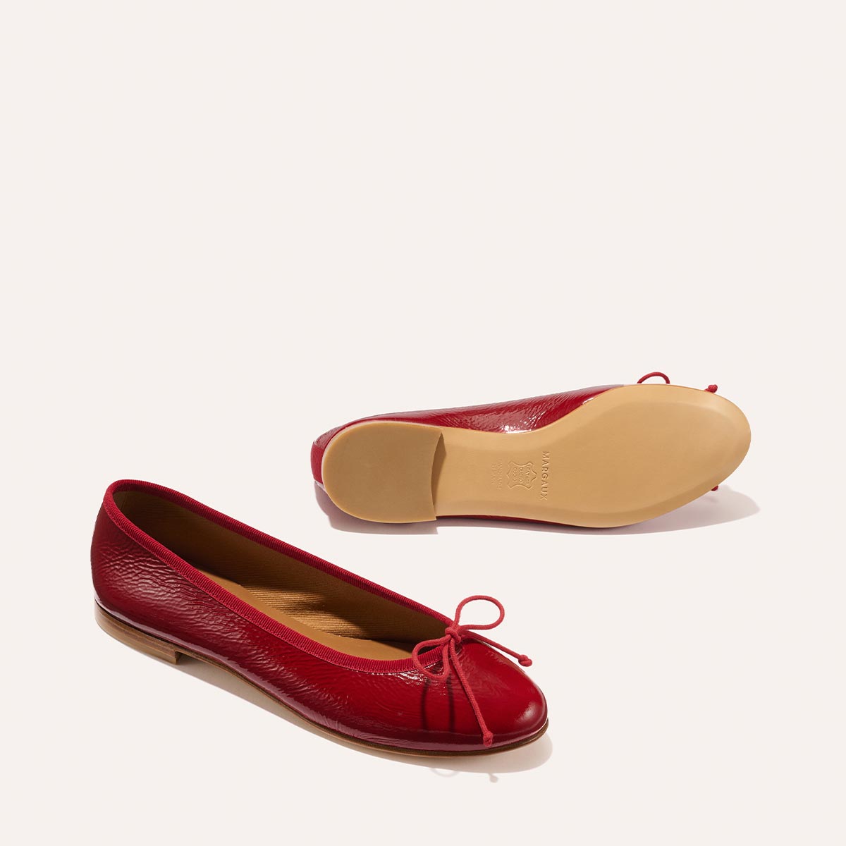 Two The Demi - Berry Crinkle Patent ballet flats by margaux-development: one upright to display the red patent upper with a bow, the other on its side to show the tan sole, both set against a plain light background.