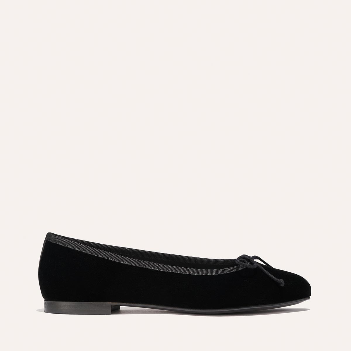 The Demi - Black Velvet by margaux-development is a black ballet flat featuring a small bow on the toe, low heel, and trim around the opening, shown against a plain light background.