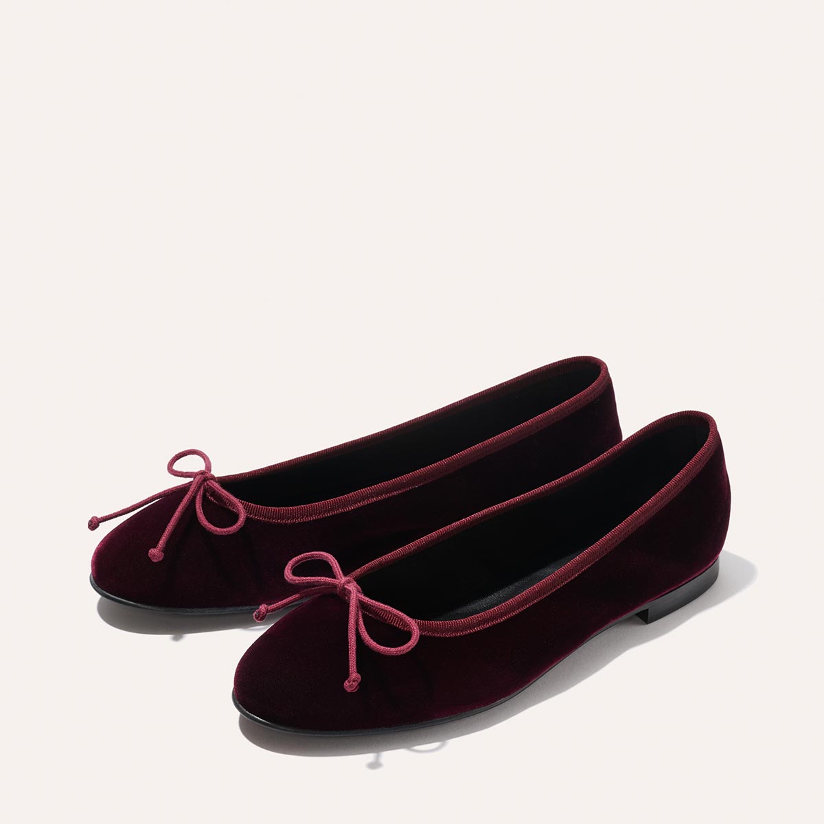The Demi - Burgundy Velvet by margaux-development: burgundy velvet ballet flats with rounded toes, pink bow accents, and flat black soles, shown on a light background.