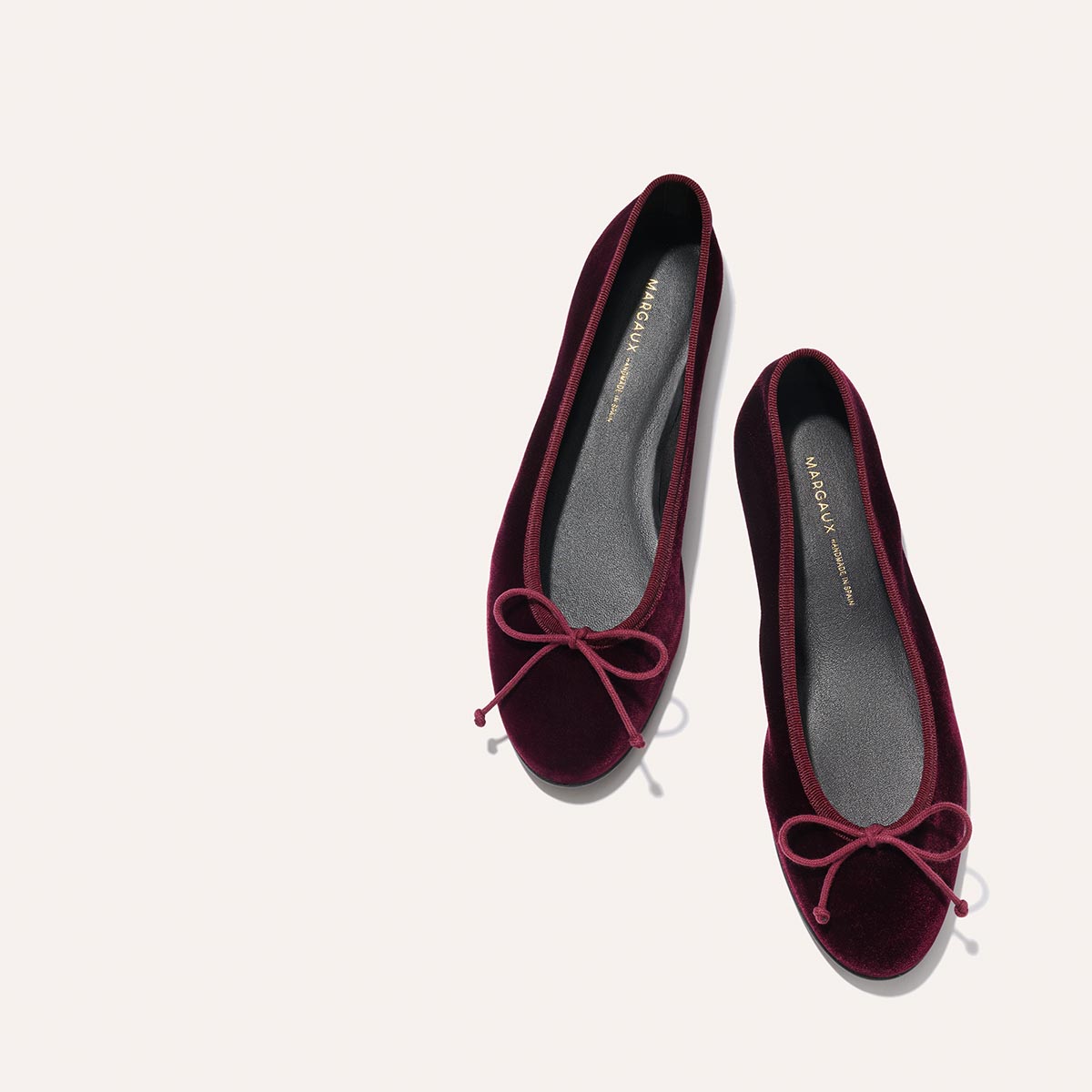 The Demi - Burgundy Velvet ballet flats by margaux-development, featuring matching bows on the toes, are shown side by side on a light neutral background.