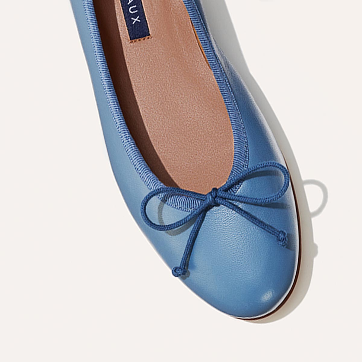 The Demi in cerulean blue nappa, a comfortable ballet flat with a rounded toe and adjustable cord bow detail.