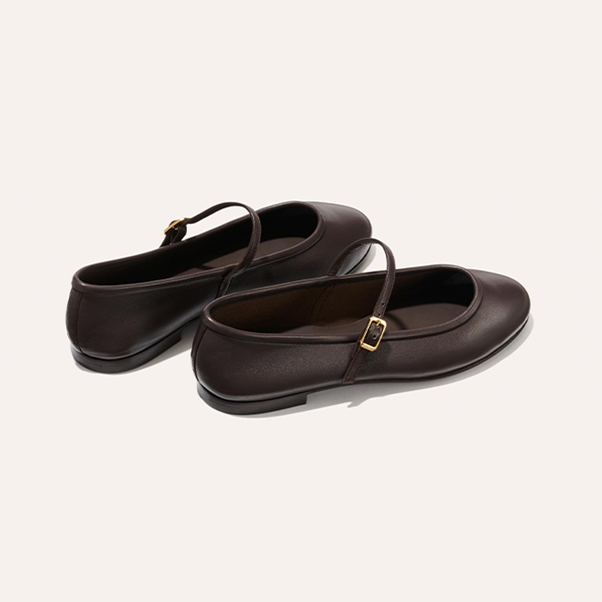 The Demi Jane - Espresso Nappa by margaux-development: dark brown leather Mary Jane flats with thin straps and gold buckles, exuding elegant femininity, displayed on a light beige background.