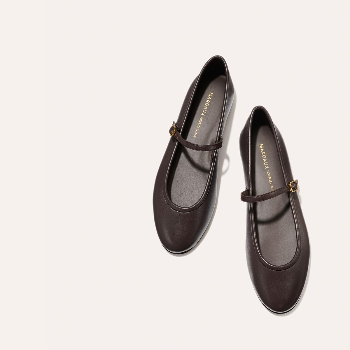 The Demi Jane - Espresso Nappa flats by margaux-development feature a single strap and gold buckle, shown on a light beige background—ideal for bringing elegant femininity to any outfit.