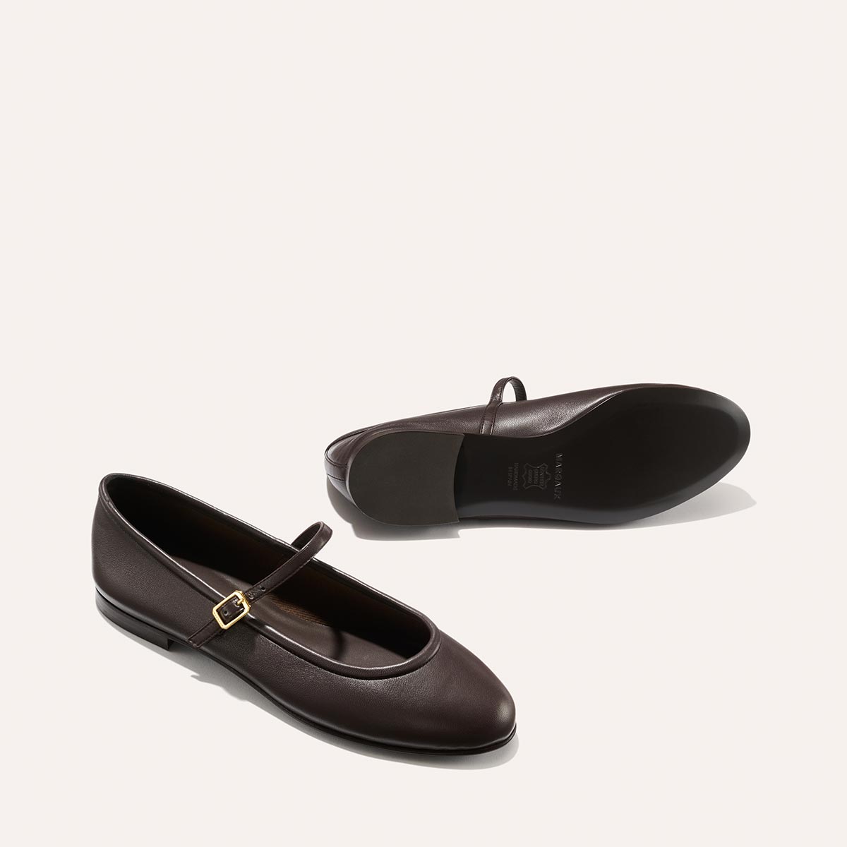 The Demi Jane - Espresso Nappa flats by margaux-development feature thin straps and gold buckles in rich dark brown leather; displayed with one upright and one on its side, they embody timeless, elegant femininity.