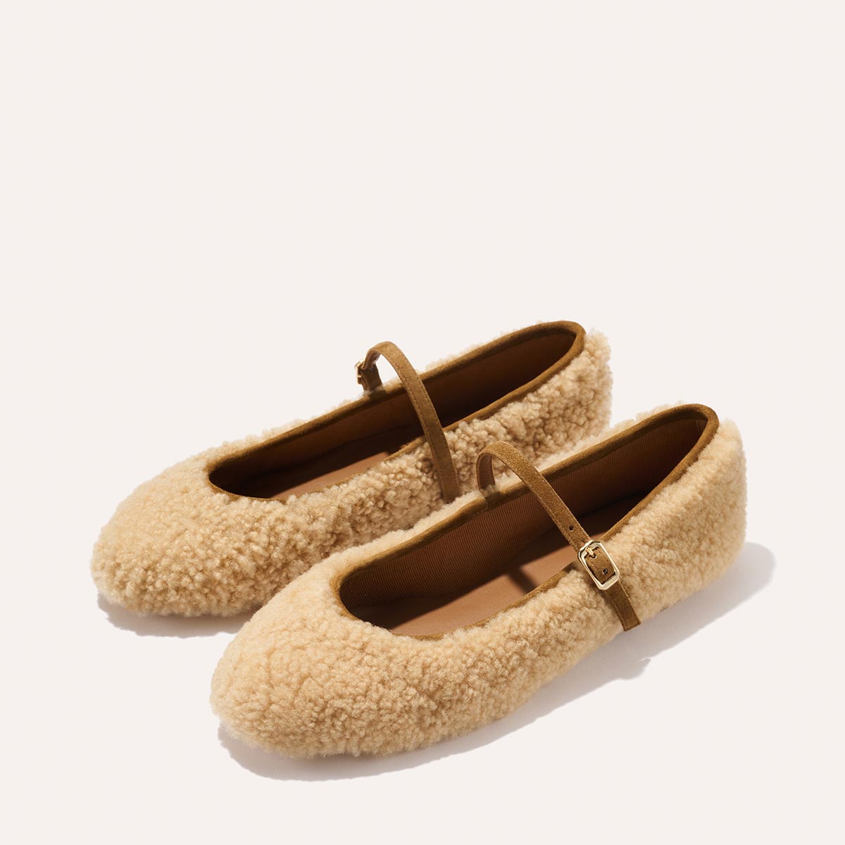 The Demi Jane - Tan Shearling flats by margaux-development feature beige fuzzy material, brown straps, and gold buckles, creating an elegantly feminine look against a neutral background.