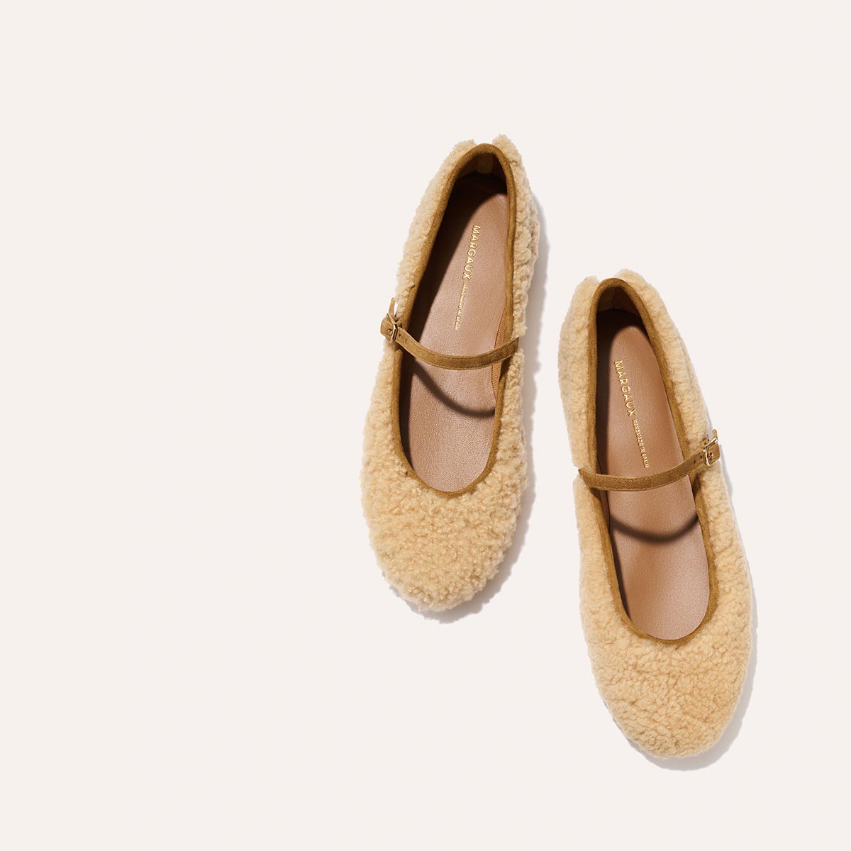 The Demi Jane - Tan Shearling by margaux-development: a pair of beige, fuzzy Mary Jane shoes with slim brown straps, set against a light background, capturing the elegant femininity of the signature Demi style.
