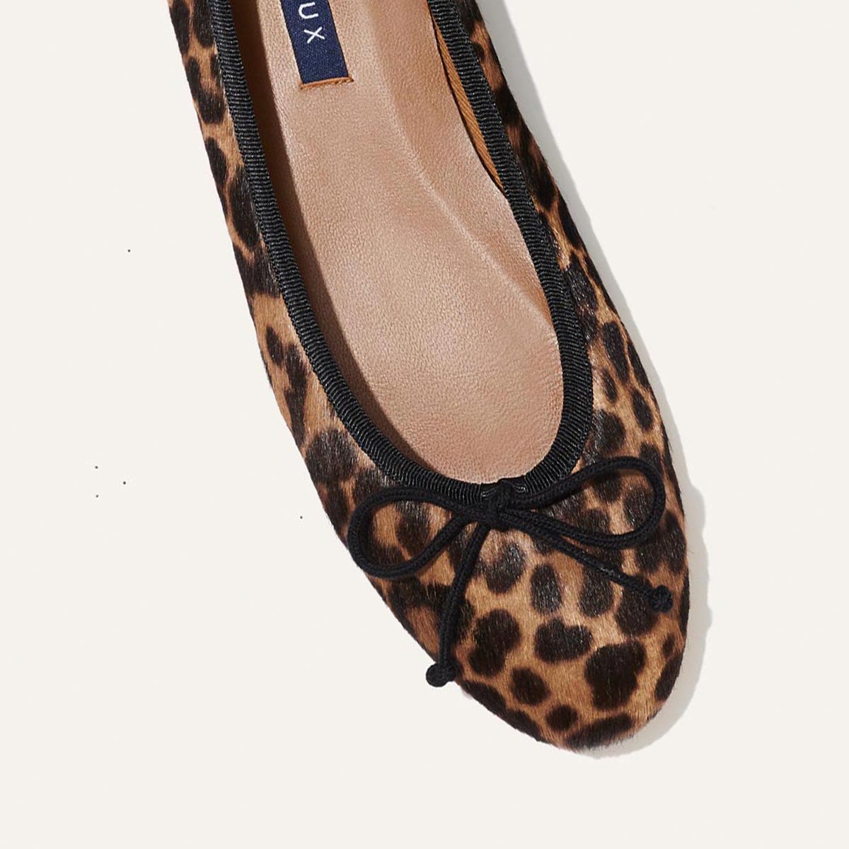 A close-up of The Demi - Chocolate Leopard Haircalf by margaux-development, a handmade Spanish ballet flat with black trim and a small black bow on the rounded toe.