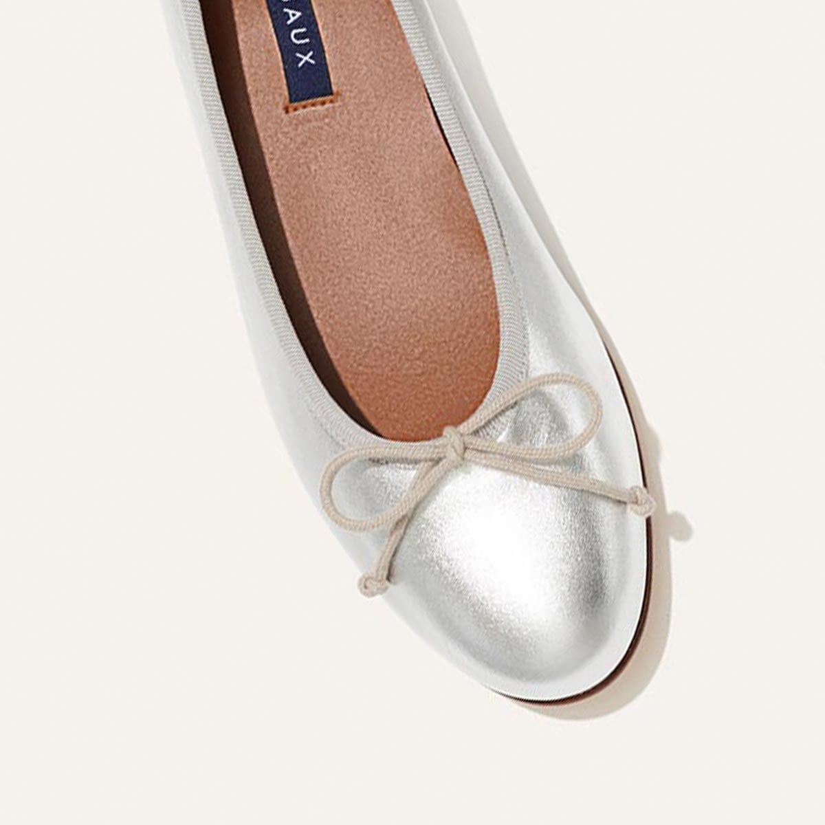The Demi in metallic Silver Nappa, a comfortable ballet flat with a rounded toe and adjustable cord bow detail.