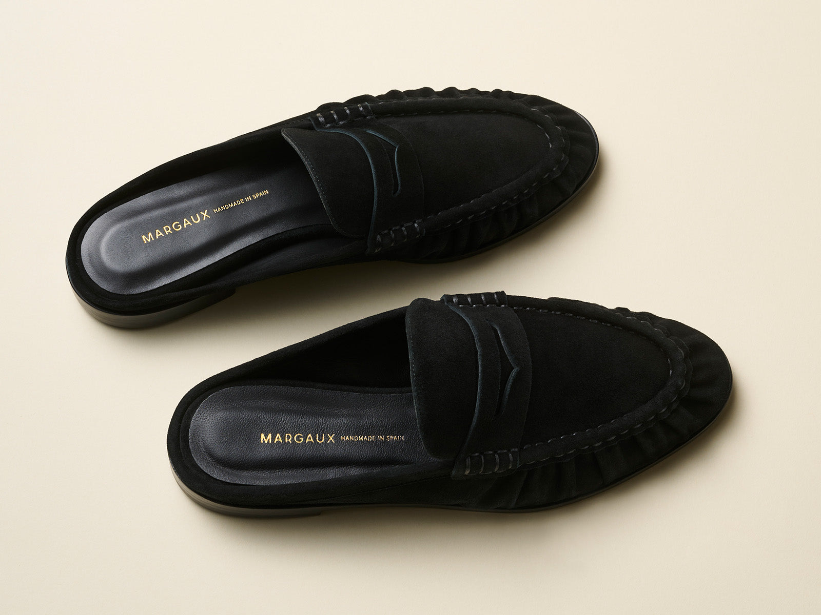 Pair of black loafers with 'MARGAUX' branding on a beige background