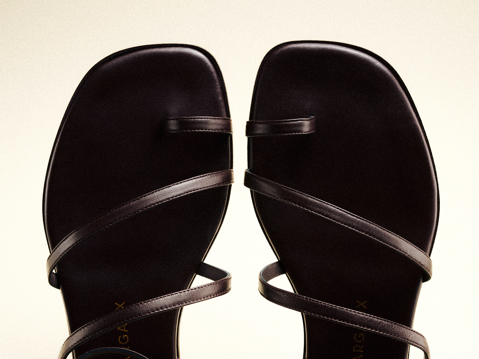 A close-up view of a pair of black, square-toed sandals with thin straps crossing over the foot and toes, set against a light background.