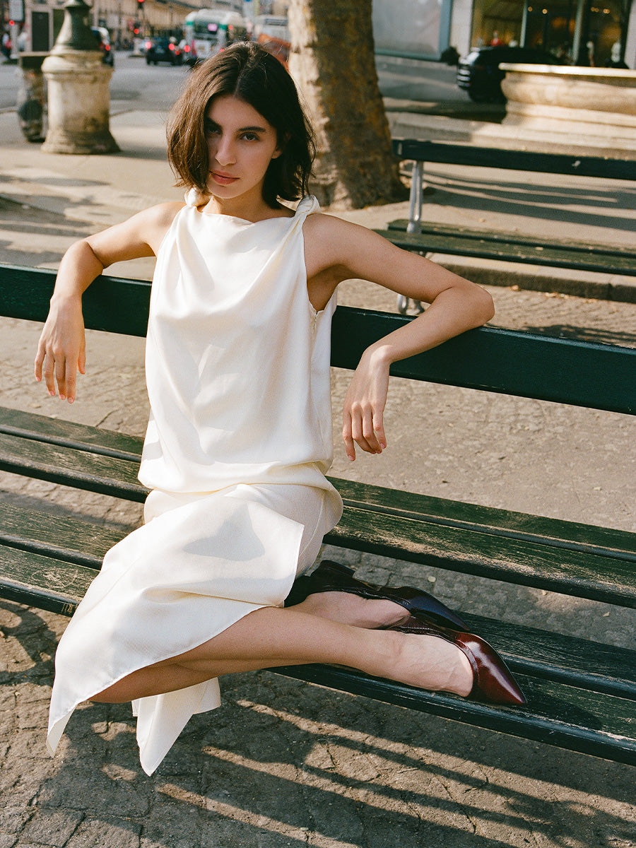 Woman in a white dress sitting on a bench outdoors