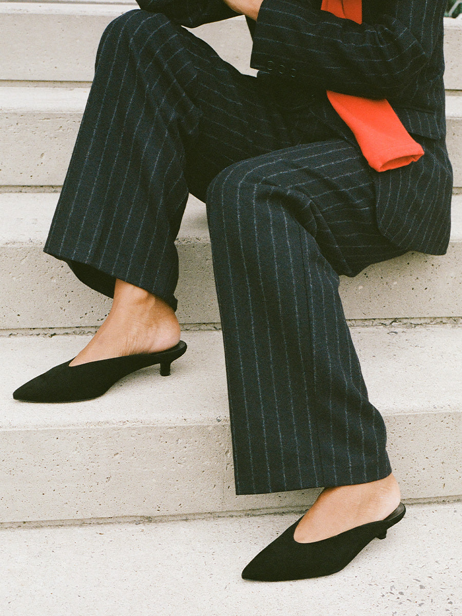 Person wearing a black pinstripe suit with a red shirt, sitting on steps.