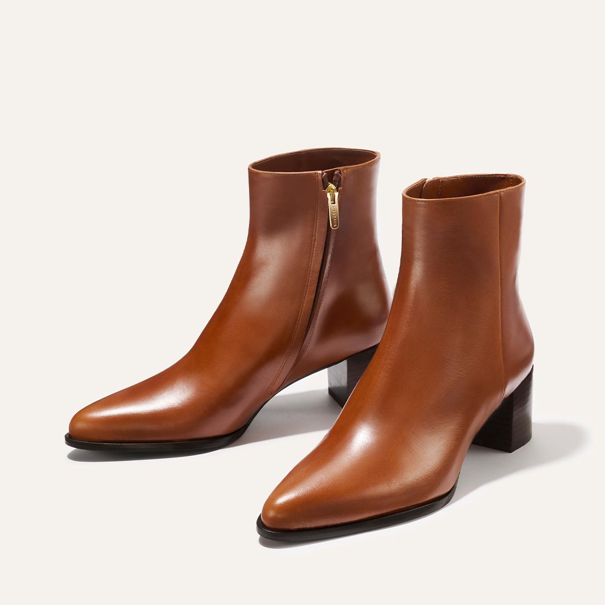 The Margaux Downtown Boot - Saddle Calf features a sleek brown western design with side zippers, pointed toes, and stacked leather heels, shown on a light background.