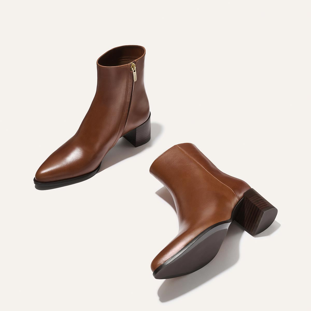 The Margaux Downtown Boot in Saddle Calf—brown leather, pointed toe ankle boots with low stacked heels and side zippers—are shown on a light background, one boot upright and the other lying on its side.