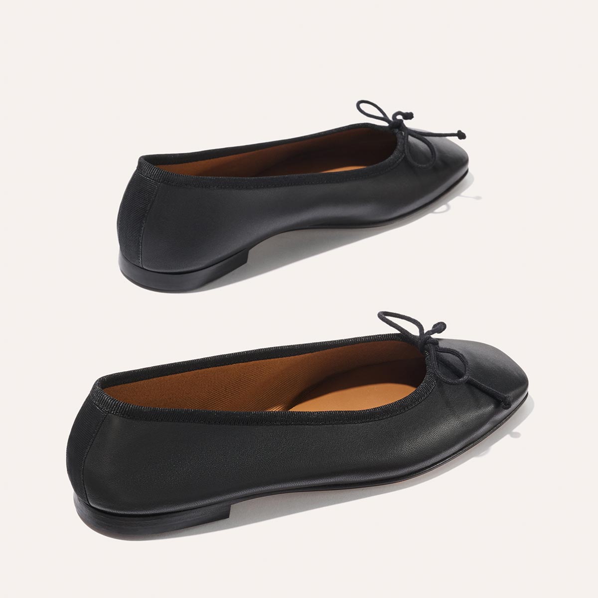 The Fonteyn - Black Nappa by Margaux: handcrafted black ballet flats with a rounded toe, low heel, bow detail, and brown lining, designed for comfort, shown on a light background.