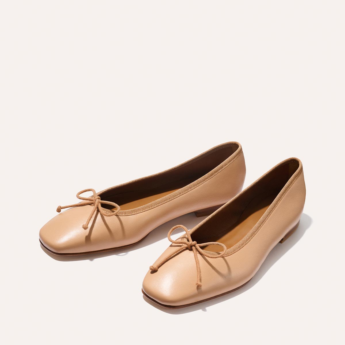 The Fonteyn - Dune Nappa by Margaux: light tan, square-toed ballet flats with low heels and front bow detail, displayed on a plain, light background.