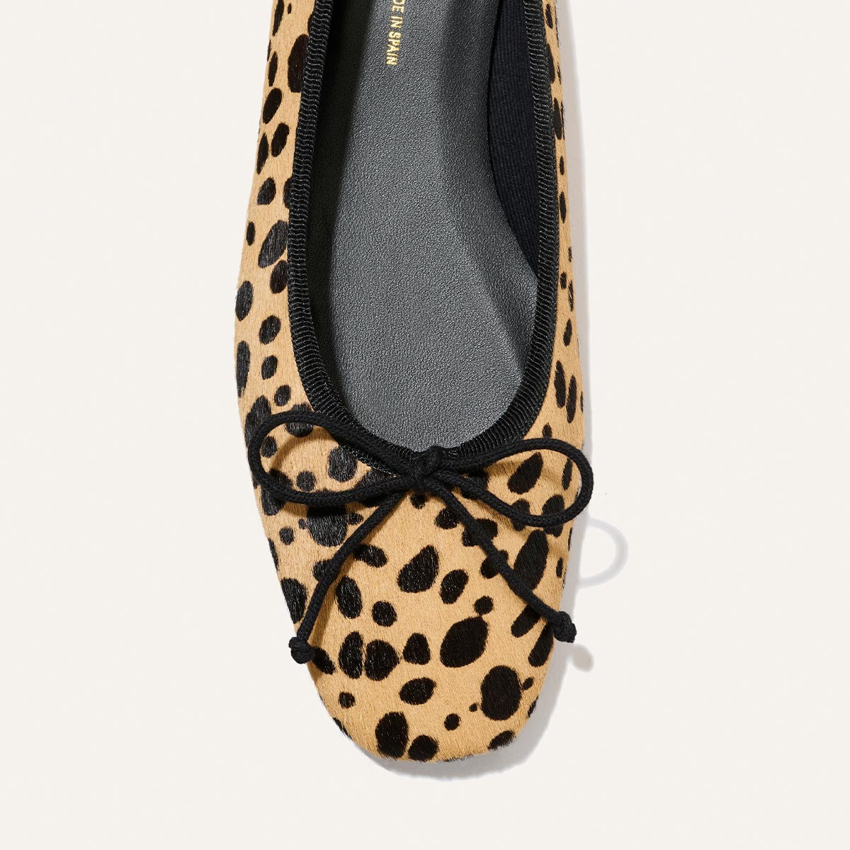 A close-up of Margaux's The Fonteyn ballet flat in tan cheetah haircalf, showcasing black trim and a black bow on the toe for a stylish yet comfort-focused design.