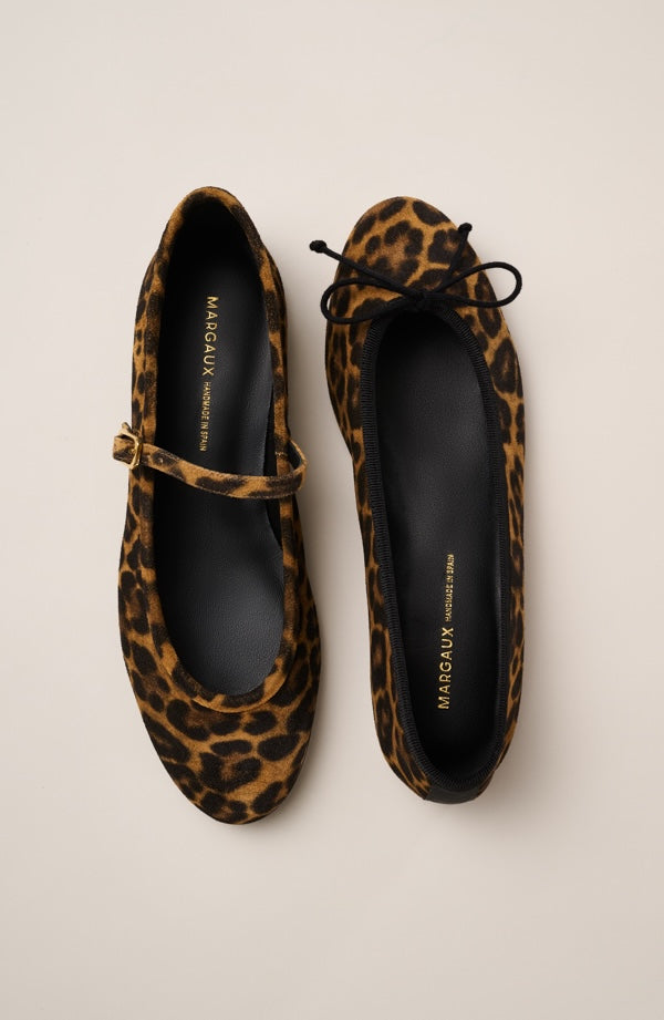 Two leopard-print Margaux ballet flats are shown on a light beige background. The left shoe has a strap across the top, while the right shoe has a bow at the front. Both have black insoles with gold branding.