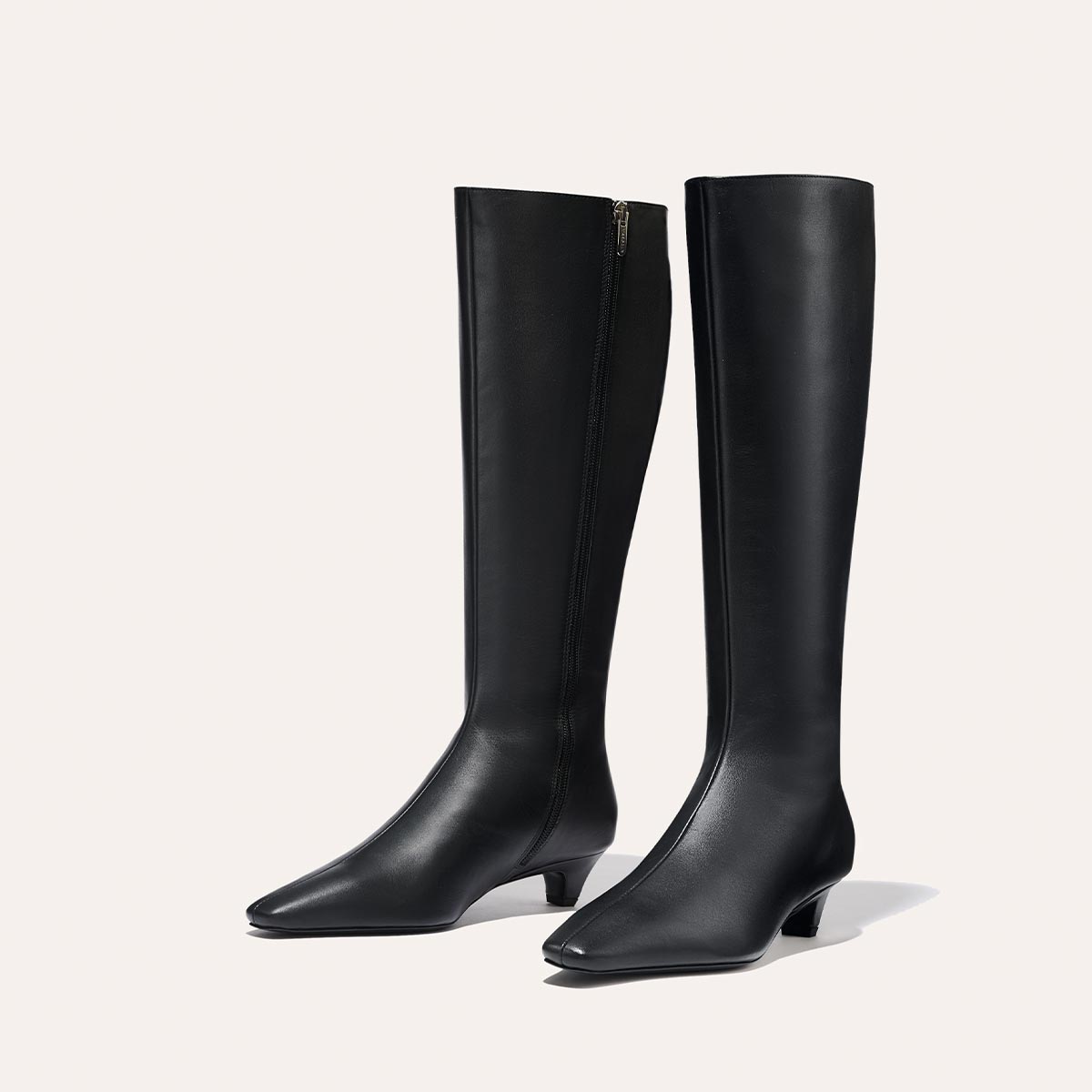 The Imogen - Black Calf by Margaux: sleek black knee-high leather boots with low heels and side zippers, shown against a plain light background.