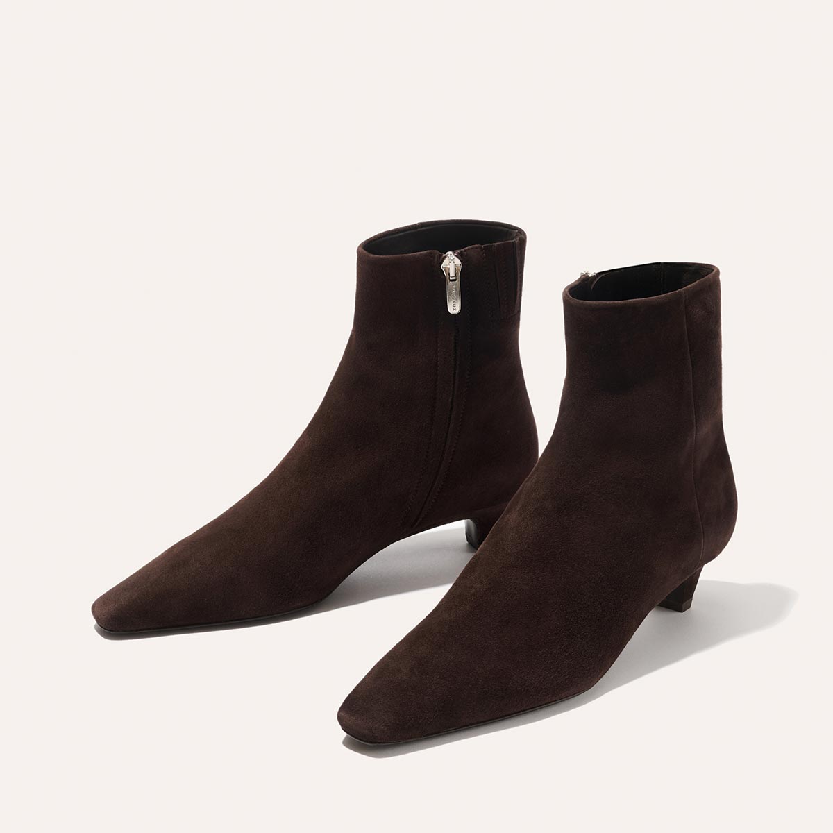 The Alex Mill x Margaux: The Inga - Espresso Suede by margaux-development features dark brown suede ankle boots with side zippers and sleek kitten heels, evoking chic New York City style, displayed on a light background.