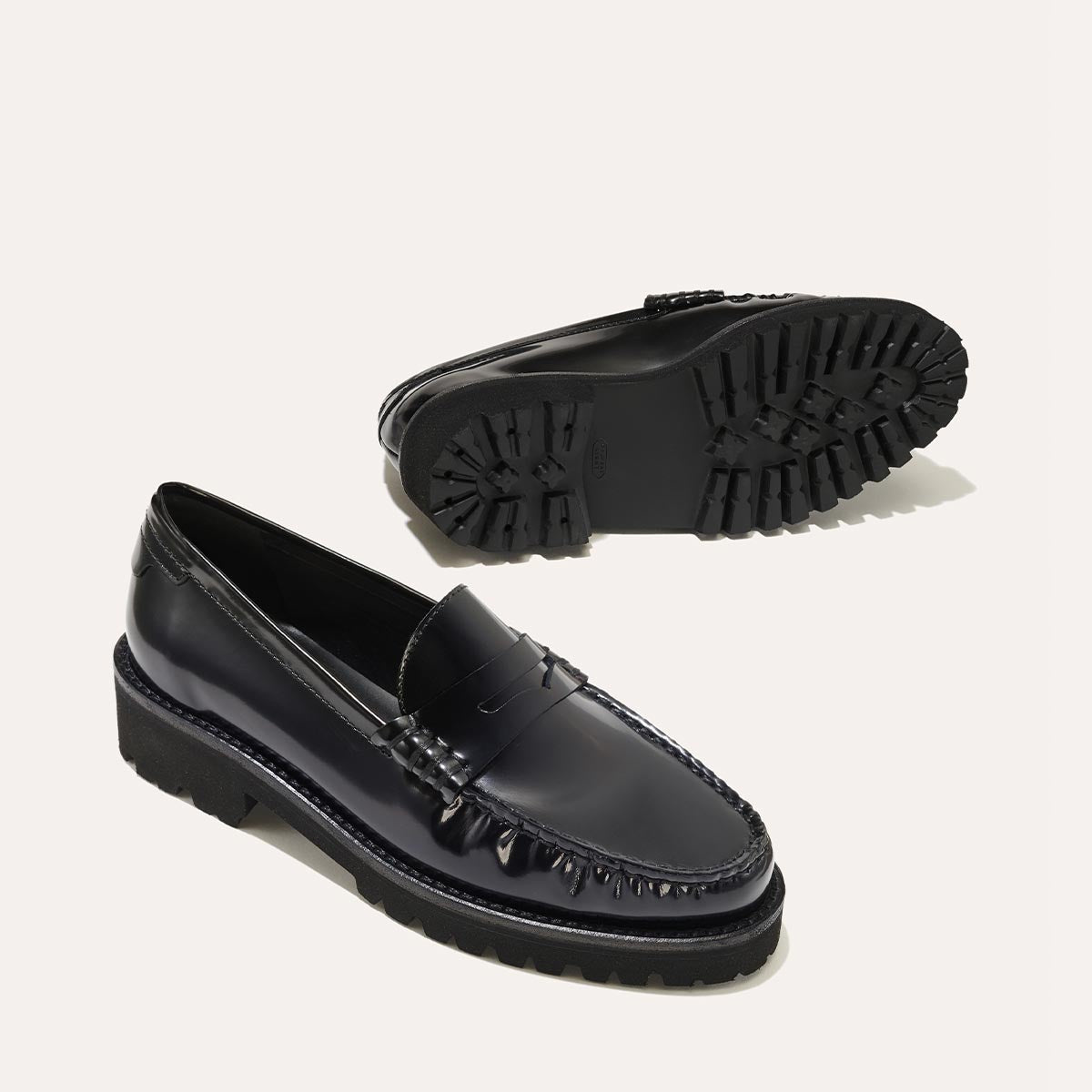 A pair of The Louisa Loafer First Edition in Black Calf by Margaux displayed with one shoe upright to show its leather lining and sleek profile, while the other is flipped to reveal the chunky, textured lug-sole tread.