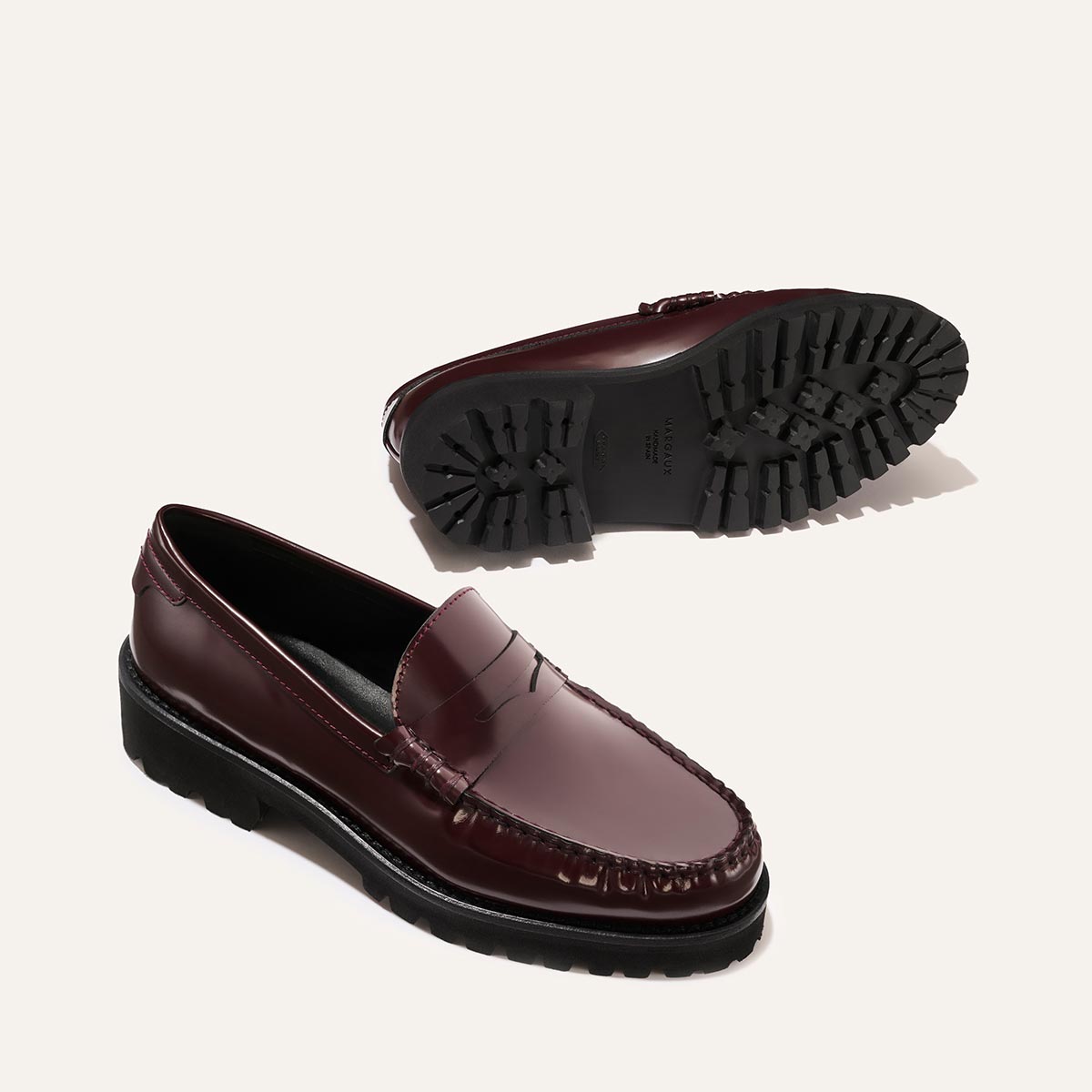 The Louisa Loafer - Burgundy Calf by Margaux features burgundy leather, black chunky lug soles, and a leather lining for comfort. Displayed from the side, one shoe shows the tread against a light beige background.