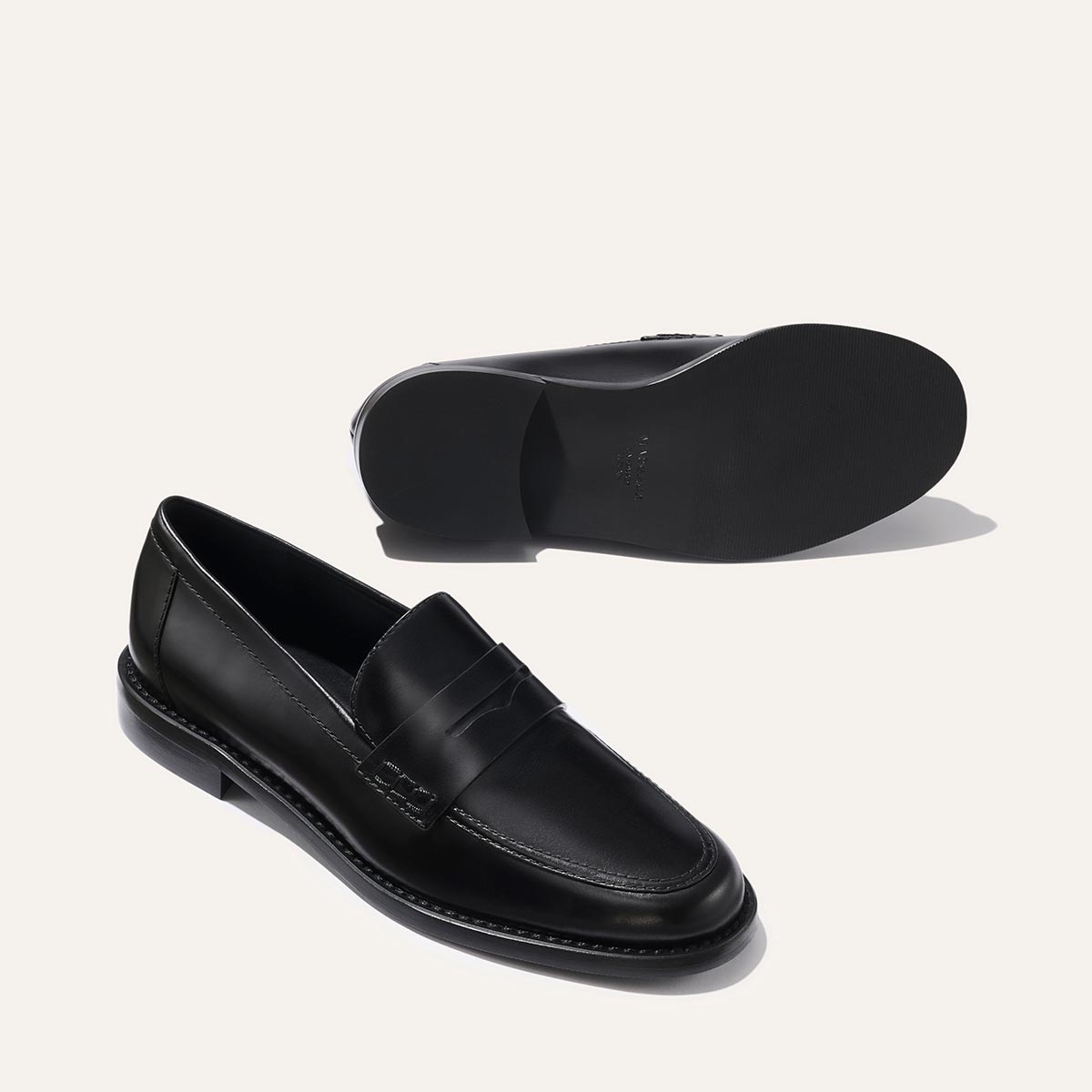 The Marlowe Loafer - Black Calf by margaux-development shown against a light background, with one loafer upright and the other on its side to display the sole.
