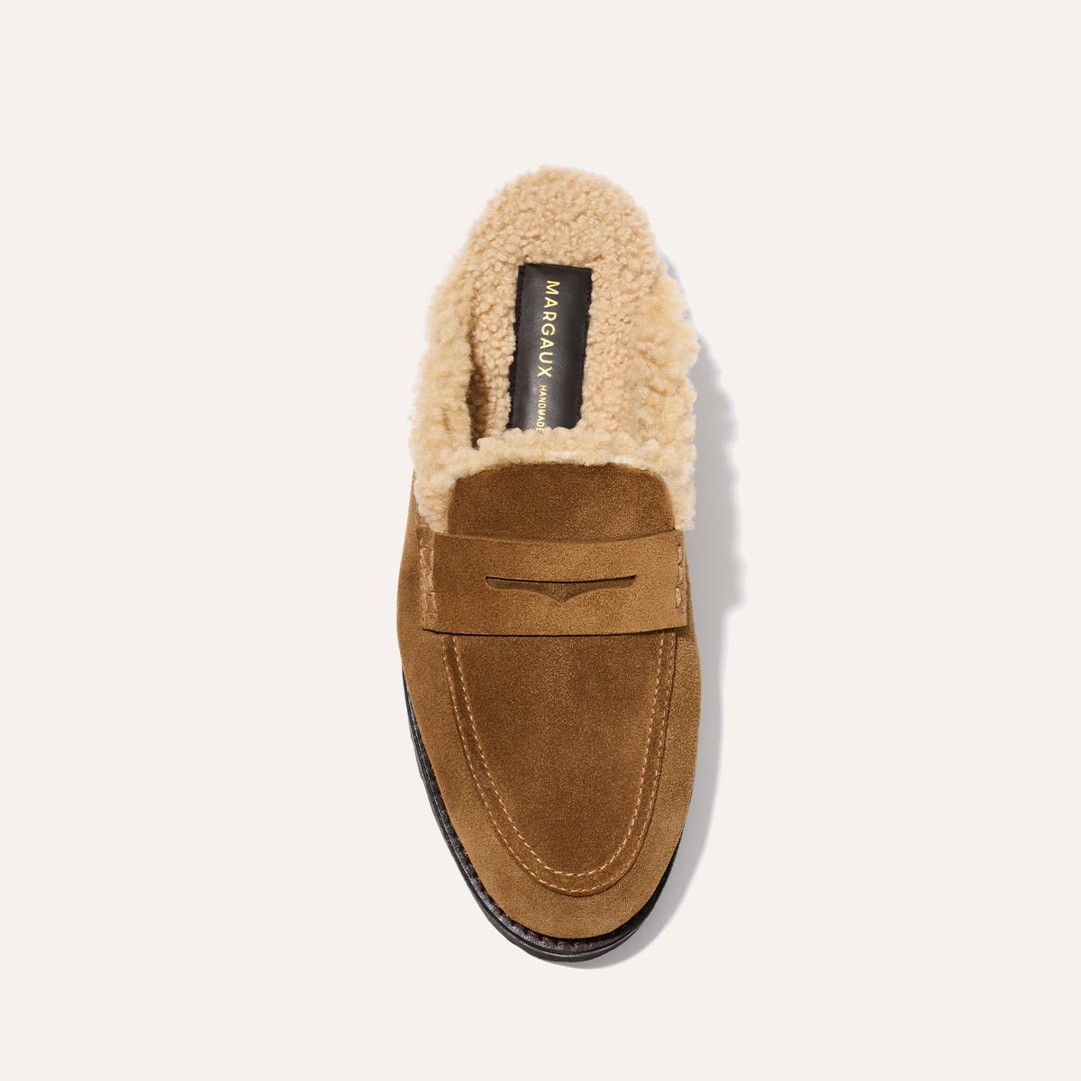 The Marlowe Mule by Margaux features walnut suede, cream shearling lining, and a leather sole. The insole displays gold "Margaux" branding. Shown from above on a light background.