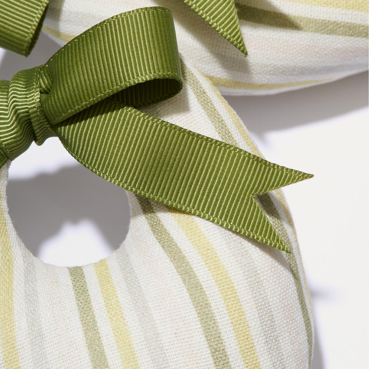 A close-up of Margaux’s Canvas Shoe Shapers from the Matilda Goad x Margaux collection, featuring soft green and beige striped fabric, a circular cutout, and a neatly tied green ribbon bow.
